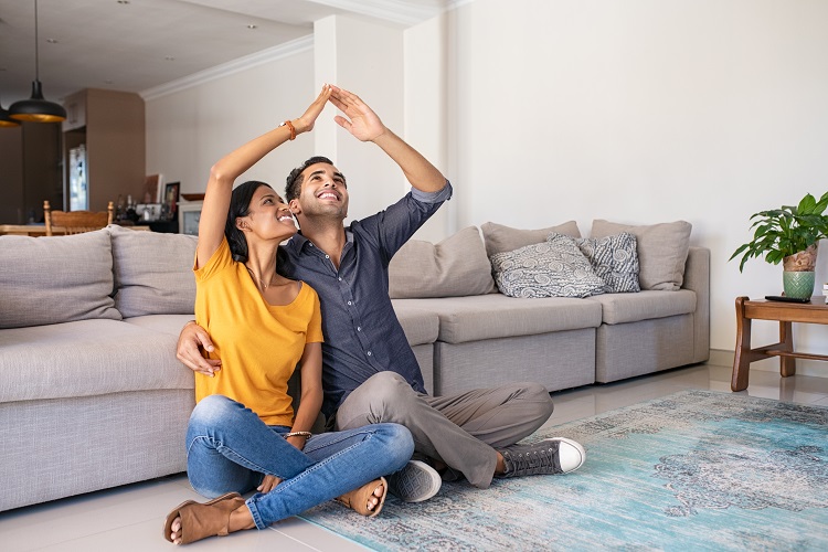 new homebuyers sitting against a gray couch in their new home