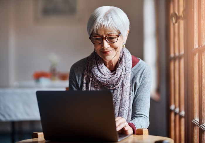 elderly woman smiling and working on a laptop